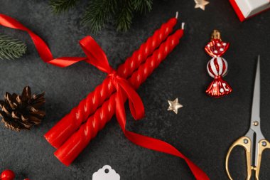 Kırmızı kurdele, kozalak, süs ve makas ile bağlanmış iki kırmızı mum.