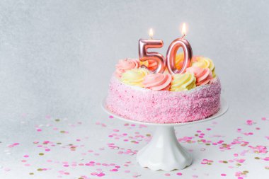 Üzerinde mumlar olan şenlikli bir pasta konfetiyle çevrili bir stantta oturur..