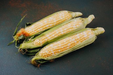 Mevsimlik tarım hasadı ya da sağlıklı yemek malzemesi fotoğrafçılığı için kabuklu üç taze mısır koçanı.