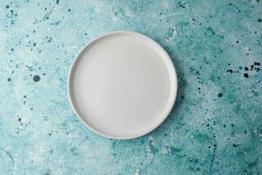 Basit bir seramik plaka, canlı boya lekeleriyle donuk bir zemine yerleştirilir..