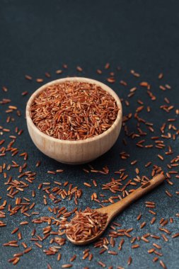 Tahta kasede kırmızı pirinç, dağınık taneler ve tahta kaşık.