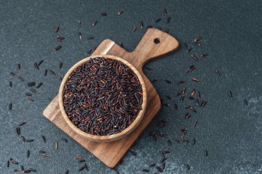 Koyu arkaplanda kesme tahtasının üzerinde tahta kasede siyah pirinç.