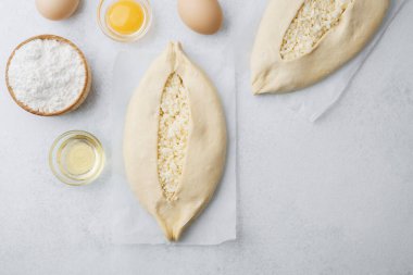 Parşömen üzerinde peynir ve fırın malzemeleri olan fırınlanmamış khachapuri.