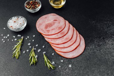 Koyu taş yüzeyde baharatlı ve otlu jambon dilimleri.