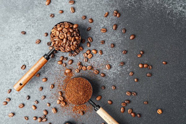 Ground coffee and beans in measuring scoops on dark background