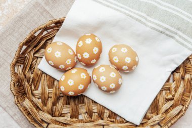 Hasır sepetinde papatya çiçekleri olan el yapımı Paskalya yumurtaları. Şenlikli kutlama için kırsal bahar kompozisyonu.