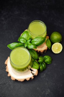 İki bardak yeşil fesleğen yaprağı ve ahşap dilimlerinde limon dilimleri olan koyu arkaplan.