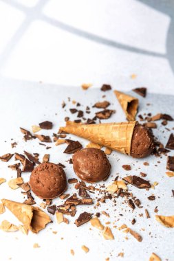 Gözleme külahlı çikolatalı dondurma kepçeleri ve arka planda çikolata parçaları.