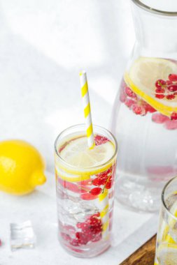 Limon dilimleri ve sarı çizgili kamışlarla servis edilen kırmızı meyveli içecek.