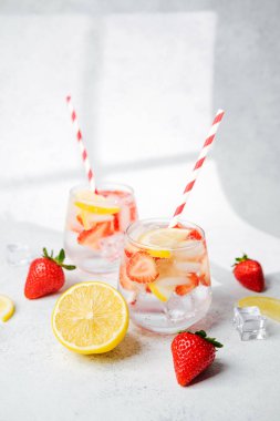 Parlak masada servis edilen buz küpleri ve çizgili kamışlarla berrak bardaklarda çilekli limonlu su.