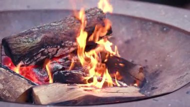 Dışarıdaki kırsal bir metal ateş çukurunda yanan odunların üzerinde parlayan sıcak kamp ateşi..
