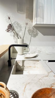 Çağdaş mutfak içinde mermer tezgah, siyah musluk, kurumuş çiçekler, güneş ışığı gölgeleri