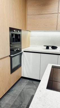 Modern mutfak, ahşap dolaplar, beyaz tezgah, fırında yapılmış, kahve makinesi, koyu fayanslar.