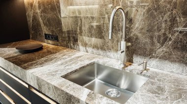 Modern mutfak tasarımı. Cilalanmış mermer yüzeyler, paslanmaz çelik lavabo, krom musluk, karanlık dolaplar..