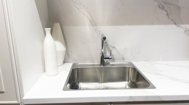 Gösterişli modern mutfak, temiz çelik lavabo, parlak musluk, beyaz mermer tezgah, arka plan, iki dekoratif vazo..