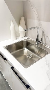 Zarif modern mutfak içinde paslanmaz çelik lavabo, beyaz mermer tezgah, krom musluk.