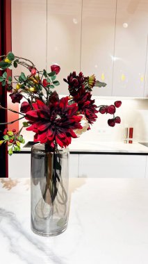 Beyaz mermer mutfak tezgahında uzun cam vazoda zarif kırmızı çiçek aranjmanı, modern ev tarzı..