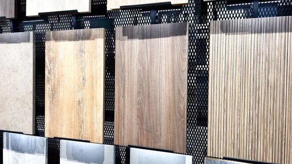 Modern bir rafta sıralanmış çeşitli seramik zemin ve duvar kiremitlerinin farklı ahşap ve taş dokularıyla görüntülenmesi.