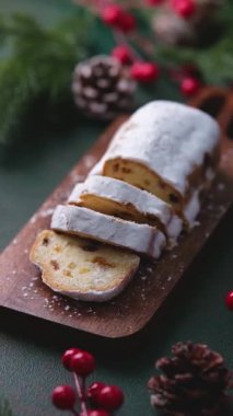 Dilimlenmiş Noel Stollen keki, tahta tahtada pudra şekeri, şenlikli dekor, kış yemeği kutlaması.