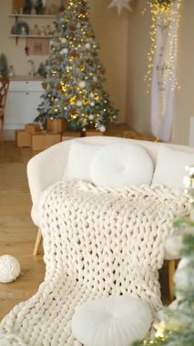 Sıcak ışıkları olan süslü bir Noel ağacının yanında kalın örgü battaniyeli rahat bir kanepe.