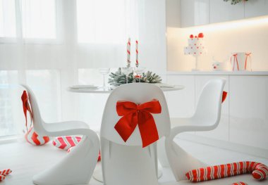 Parlak minimalist bir odada kırmızı fiyonklarla süslenmiş beyaz sandalyeler ve baston şekerler..