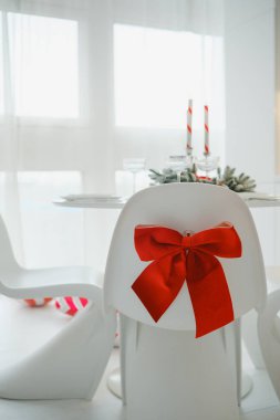 Mumlar ve yeşilliklerle süslenmiş kırmızı fiyonklarla süslenmiş beyaz sandalyeler..