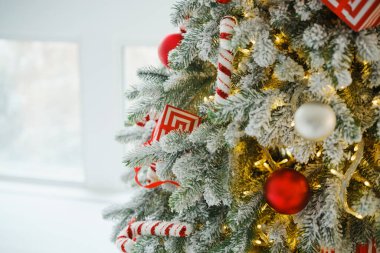 Kırmızı mücevherler, baston şekerler ve ışıklarla süslenmiş yeşil çam ağaçları.