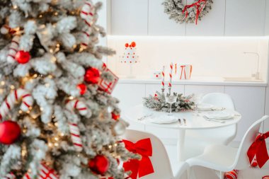 Parlak mutfakta süslü ağaç ve şenlikli çelenkli şık bir Noel sofrası.