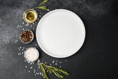 Siyah taş zemin üzerinde bitkiler ve baharatlar olan boş beyaz tabak