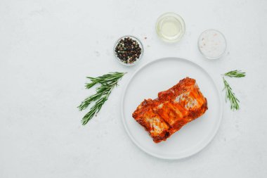 Beyaz tabakta marine edilmiş domuz pirzolası, biberiye ve baharatlı.