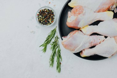 Biberiye ve baharatlı siyah tabakta çiğ tavuk budu.