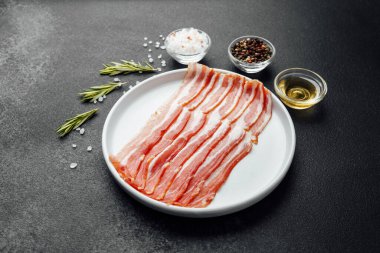 Beyaz tabakta çiğ domuz pastırması, biber, tuz ve biberiye.