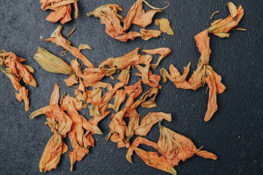 Kurumuş turuncu zambak yaprakları koyu dokulu bir yüzeye saçılmış, yukarıdan aşağıya doğru..