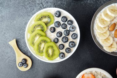 Kivili yulaf ezmesi kasesi ve böğürtlenli ve çeşitli meyveli siyah masa.