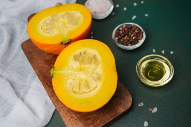 Koyu yeşil bir yüzey üzerinde baharat ve yağla ahşap bir tahtanın üzerinde ikiye bölünmüş turuncu balkabağı.