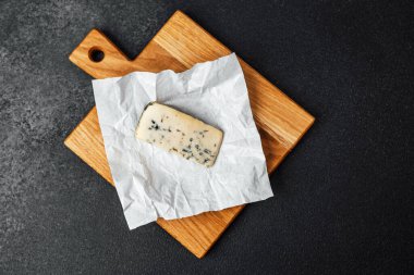 Parşömene sarılı leziz mavi peynir ahşap bir kesme tahtasının üzerinde duruyor..