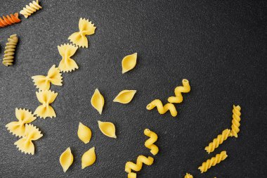 Makarnanın farklı şekilleri ve renkleri zarif bir şekilde siyah bir yüzeye dağılmış..