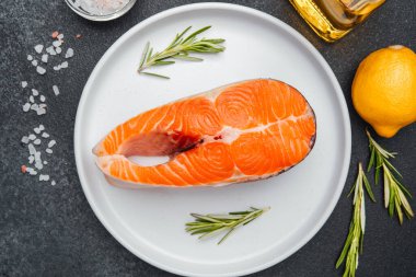 Limon ve biberiyeyle süslenmiş somon bifteği pişirmeye hazır beyaz bir tabakta oturur..