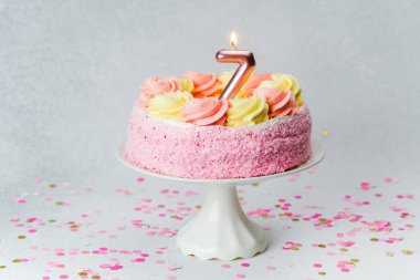 Festivalsel bir pasta üzerinde tek bir mum bulunan pembe ve sarı kıvrımlara sahiptir..