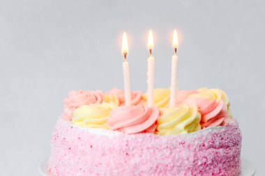 Sarı ve pembe kremalı canlı pembe bir pasta üç mum yakar..