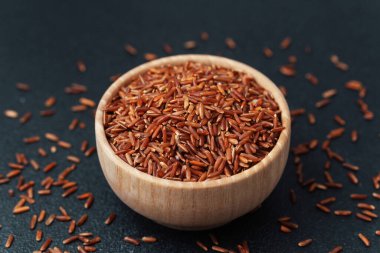 Koyu arka planda dağınık tanecikler olan ahşap kasede kırmızı pirinç yakın plan.