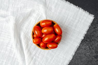 Canlı vişneli domateslerle dolu bir kase beyaz bir bezin üzerinde, tabakta kullanılmaya hazır..