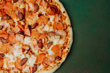 Sıcak ve peynirli biberli pizza yeşil bir zeminde oturur, paylaşmak için mükemmeldir..