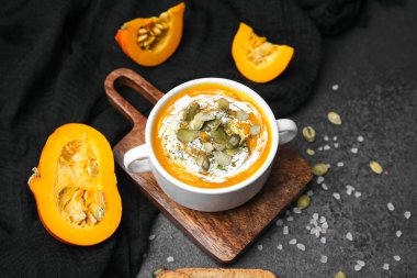 Krema ve çekirdekli kabak çorbası, koyu arkaplanda taze balkabağı parçaları ile servis edilir..
