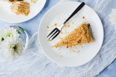 Kremalı Napolyon keki ve beyaz tabakta beyaz çatal ve beyaz çiçeklerle.