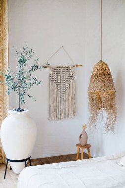 Büyük beyaz saksı bitkisi, makrome duvar asılı, dokuma ışık ve seramik vazo ile sıcak boho oda dekoru.