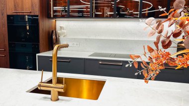 Altın musluğu, beyaz mermer tezgahı, koyu dolapları, zarif sonbahar yaprakları olan modern lüks mutfak..