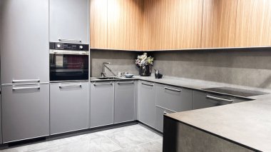 Modern mutfak, parlak gri dolaplar, dahili fırın, ahşap dolaplar, ve büyük gri tezgah..