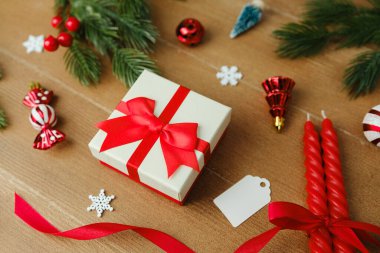 Kırmızı kurdeleli hediye kutusu, çam dalları, mumlar ve ahşap süslerle süslenmiş.