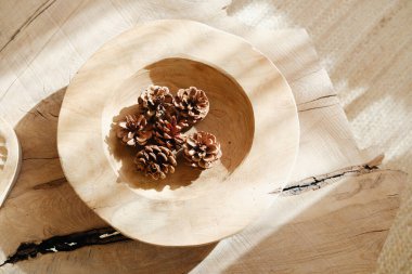 Doğal çam kozalakları yumuşak gölgeli dokulu bir yüzeyde, ahşap bir kasede dinlenir.